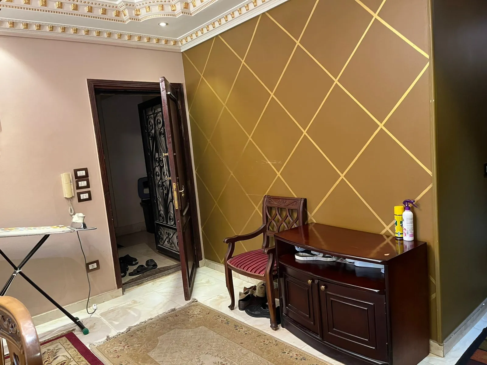 Entry with a gold diamond-pattern wall and a wooden cabinet - apartment in Banafseg Buildings, New Cairo