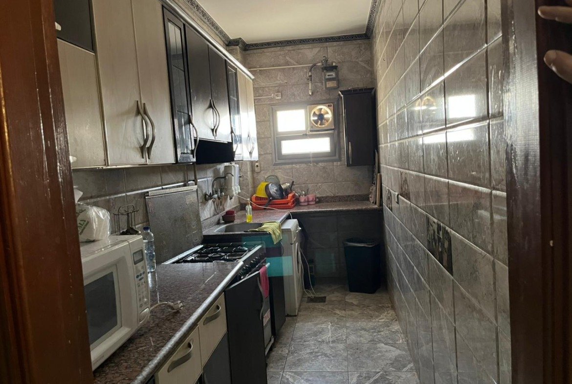 Narrow kitchen with a dark counter, microwave and wall tiles - apartment in Banafseg Buildings, New Cairo