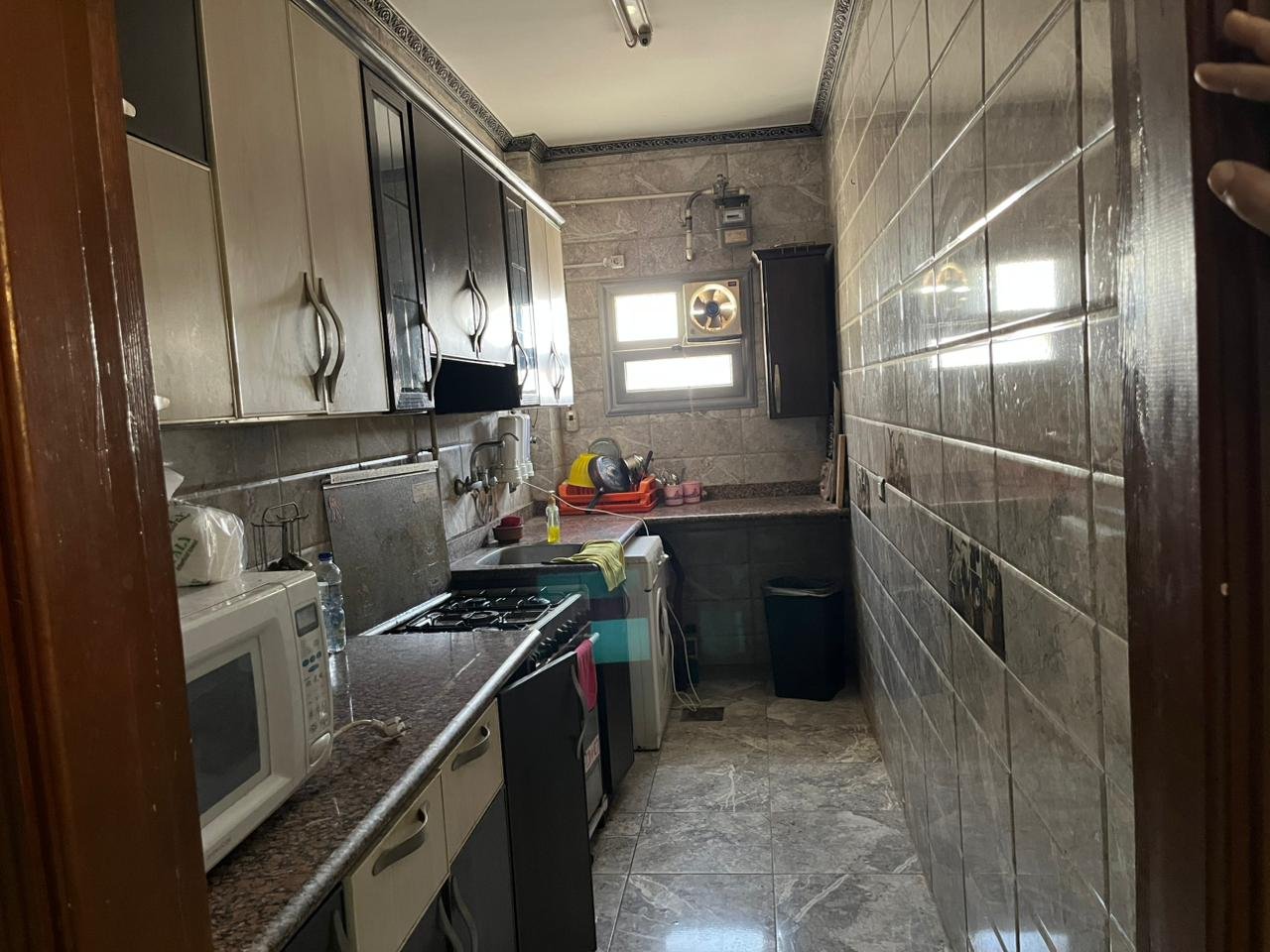 Narrow kitchen with a dark counter, microwave and wall tiles - apartment in Banafseg Buildings, New Cairo