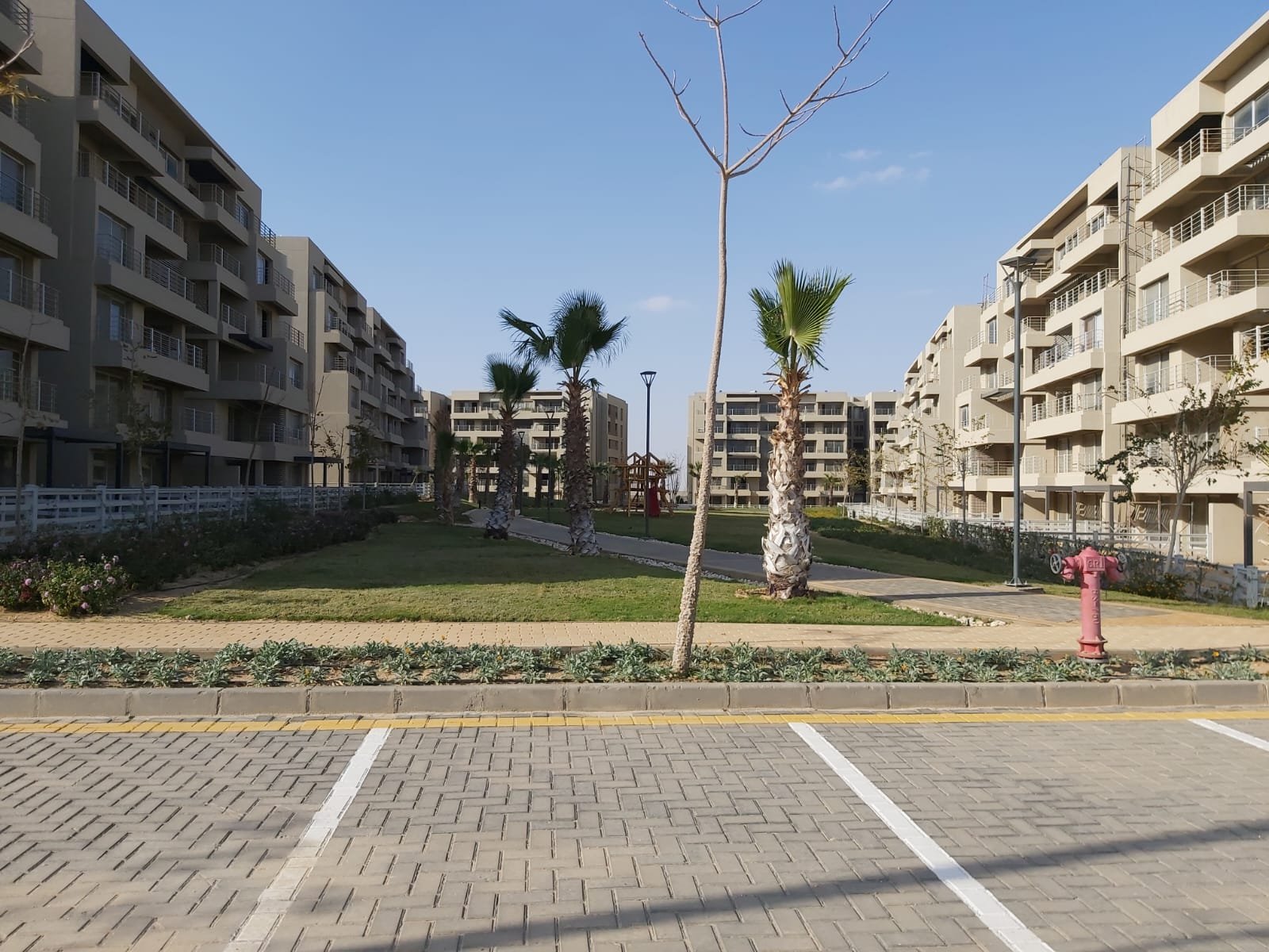 capital-gardens-mostakbal-city-compound-2 صف مواقف أمام بلوكات سكنية مع نخيل وشجرة صغيرة - شقة في كابيتال جاردنز بجوار مدينتي، مدينة المستقبل