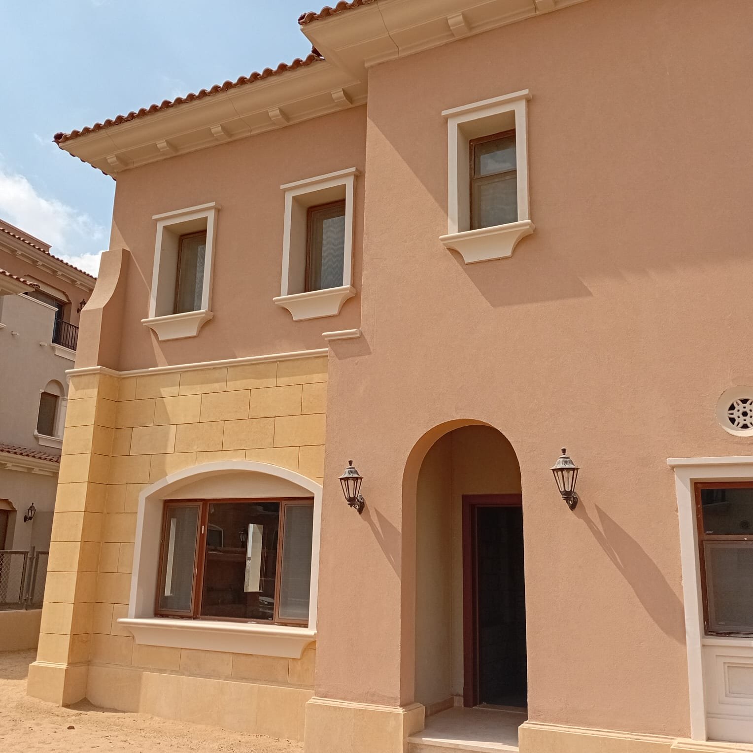 واجهة فيلا كواترو للبيع في سيتي جيت التجمع الخامس Villa entrance with an arched door and a stone window frame - villa in CityGate, New Cairo