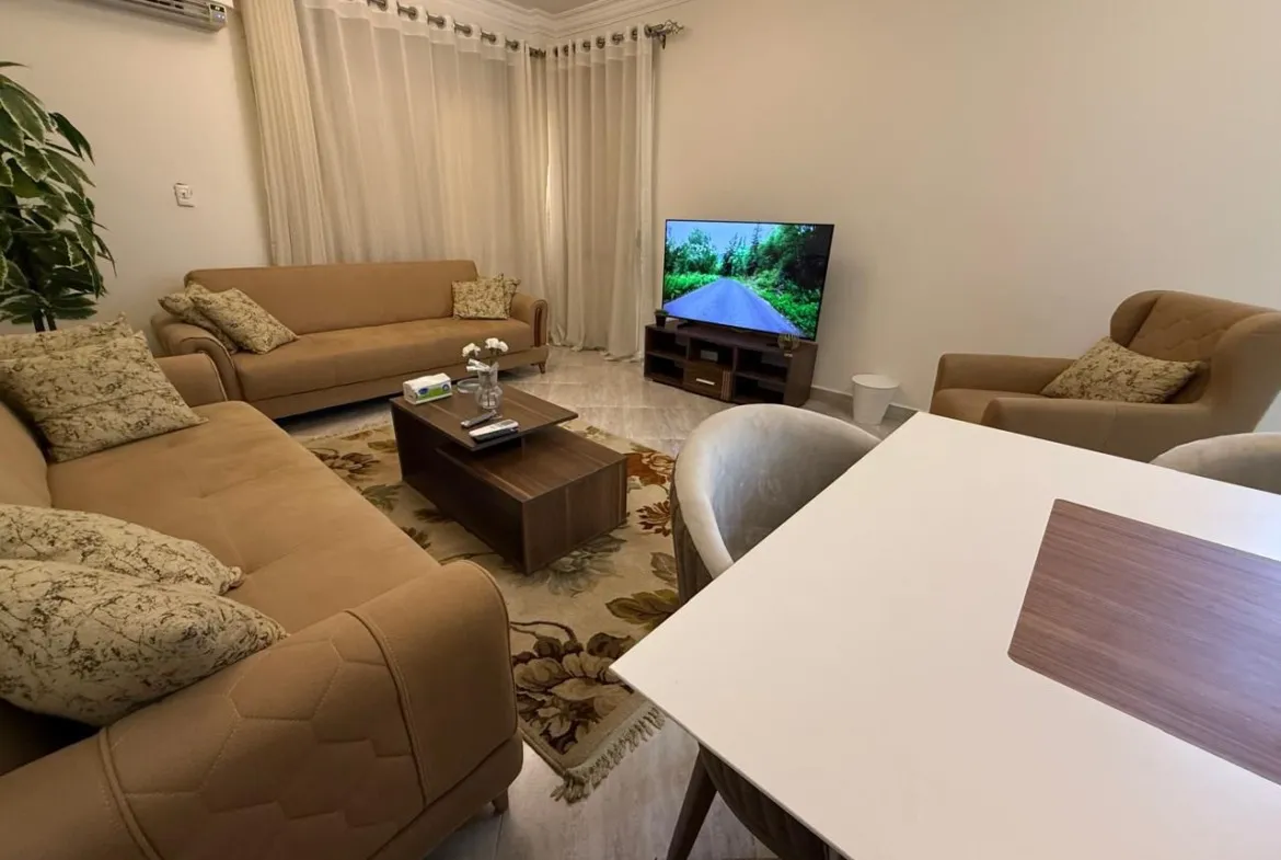 Living room with tan sofas, a coffee table and wall TV - apartment in Dar Misr Al Koronfol New Cairo – 3 Bedrooms 130 sqm, New Cairo
