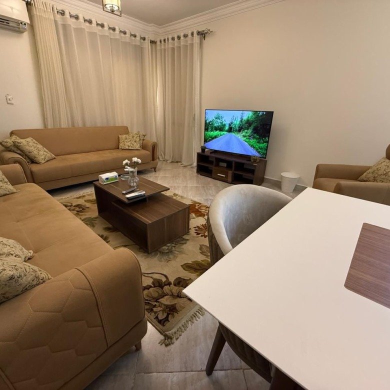 Living room with tan sofas, a coffee table and wall TV - apartment in Dar Misr Al Koronfol New Cairo – 3 Bedrooms 130 sqm, New Cairo