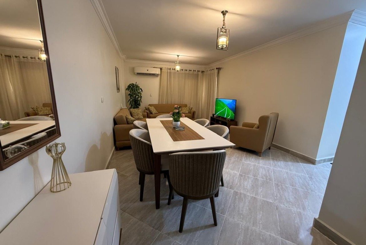 Dining table with grey chairs beside the living area - apartment in Dar Misr Al Koronfol New Cairo – 3 Bedrooms 130 sqm, New Cairo