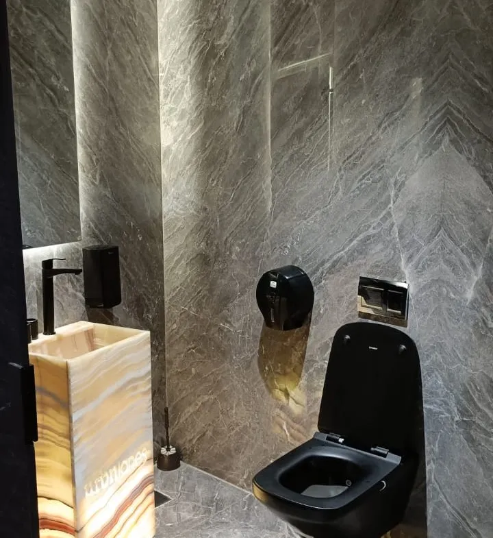 Guest bathroom with a black toilet and a lit stone wall - unit in Marassi