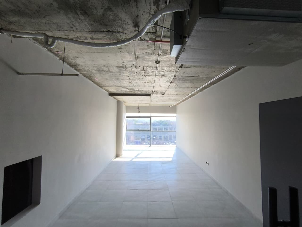 Narrow bare shell unit with an exposed concrete ceiling and a window at the end - unit in Marassi