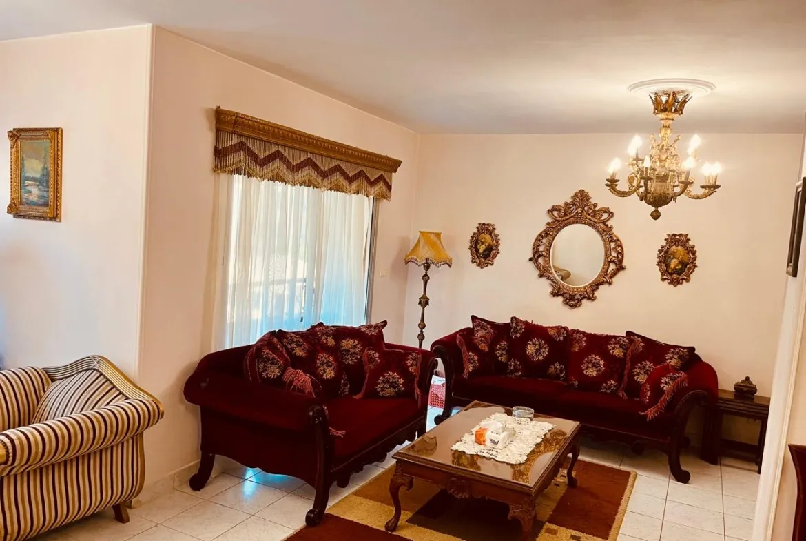 Living room with burgundy sofas, a gilt mirror and chandelier - apartment in El Rehab New Cairo – 3 Bedrooms 183 sqm – Garden View, New Cairo