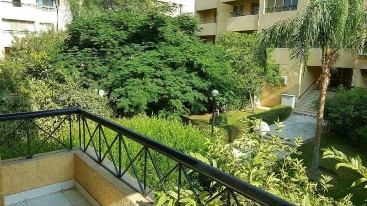Green courtyard and palms behind a metal balcony railing - apartment in El Rehab New Cairo – 3 Bedrooms 183 sqm – Garden View, New Cairo