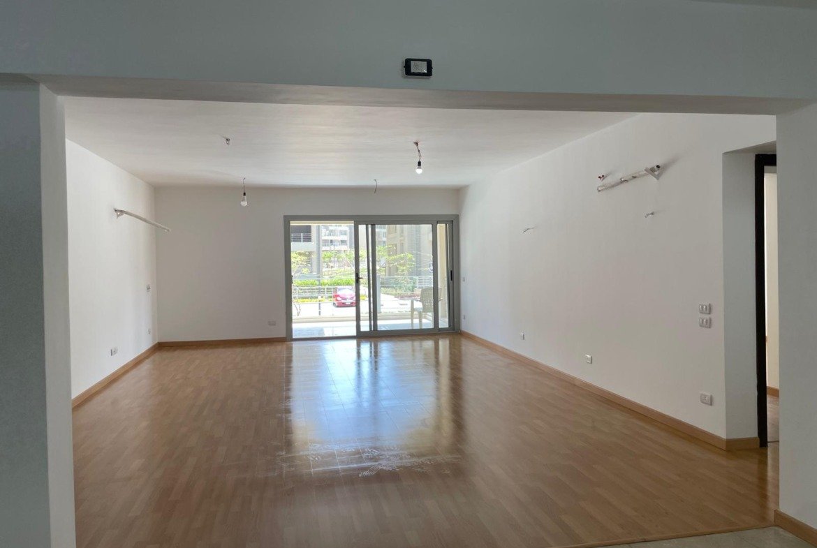 Empty living room with a wooden floor and a sliding door to the terrace - apartment in Capital Gardens Next to Madinaty, Mostaqbal City