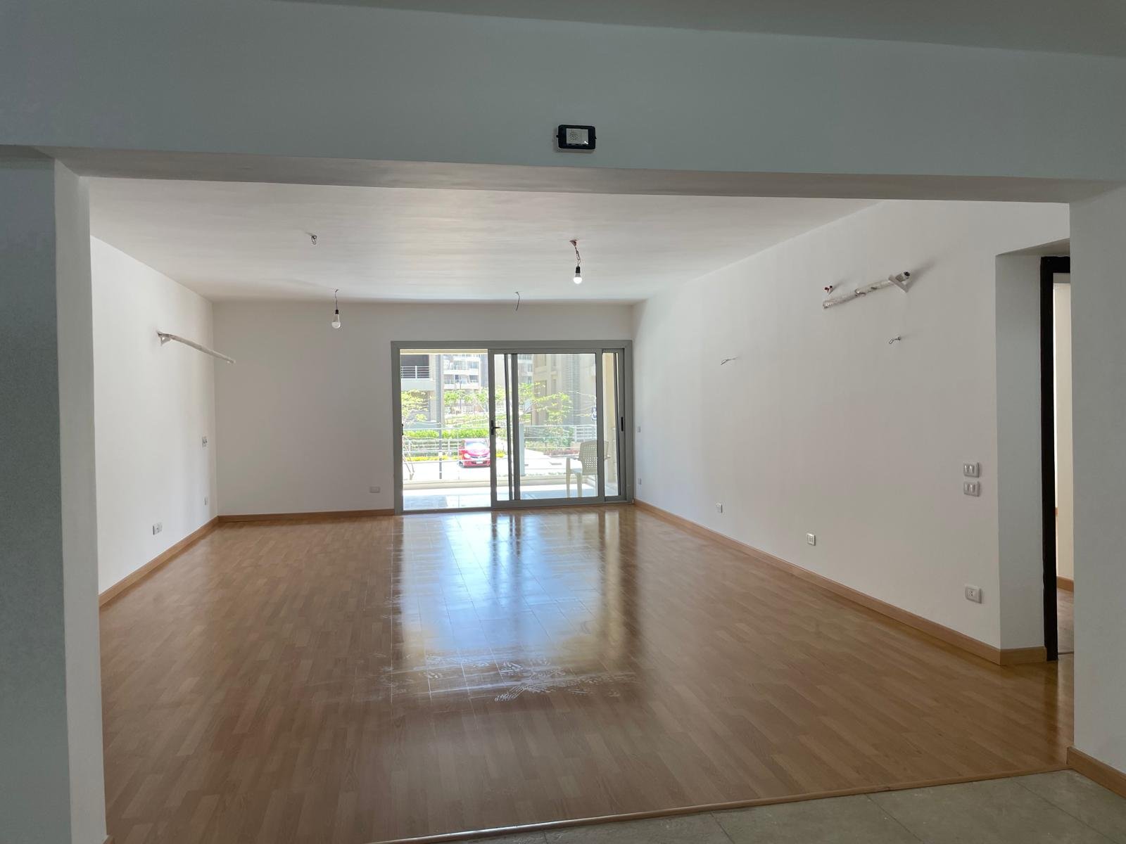 Empty living room with a wooden floor and a sliding door to the terrace - apartment in Capital Gardens Next to Madinaty, Mostaqbal City