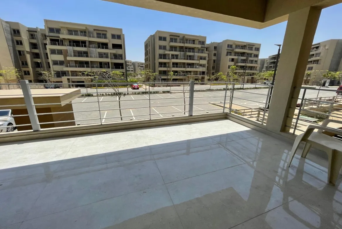 Covered terrace with a glass railing overlooking residential buildings and a car park - apartment in Capital Gardens Next to Madinaty, Mostaqbal City