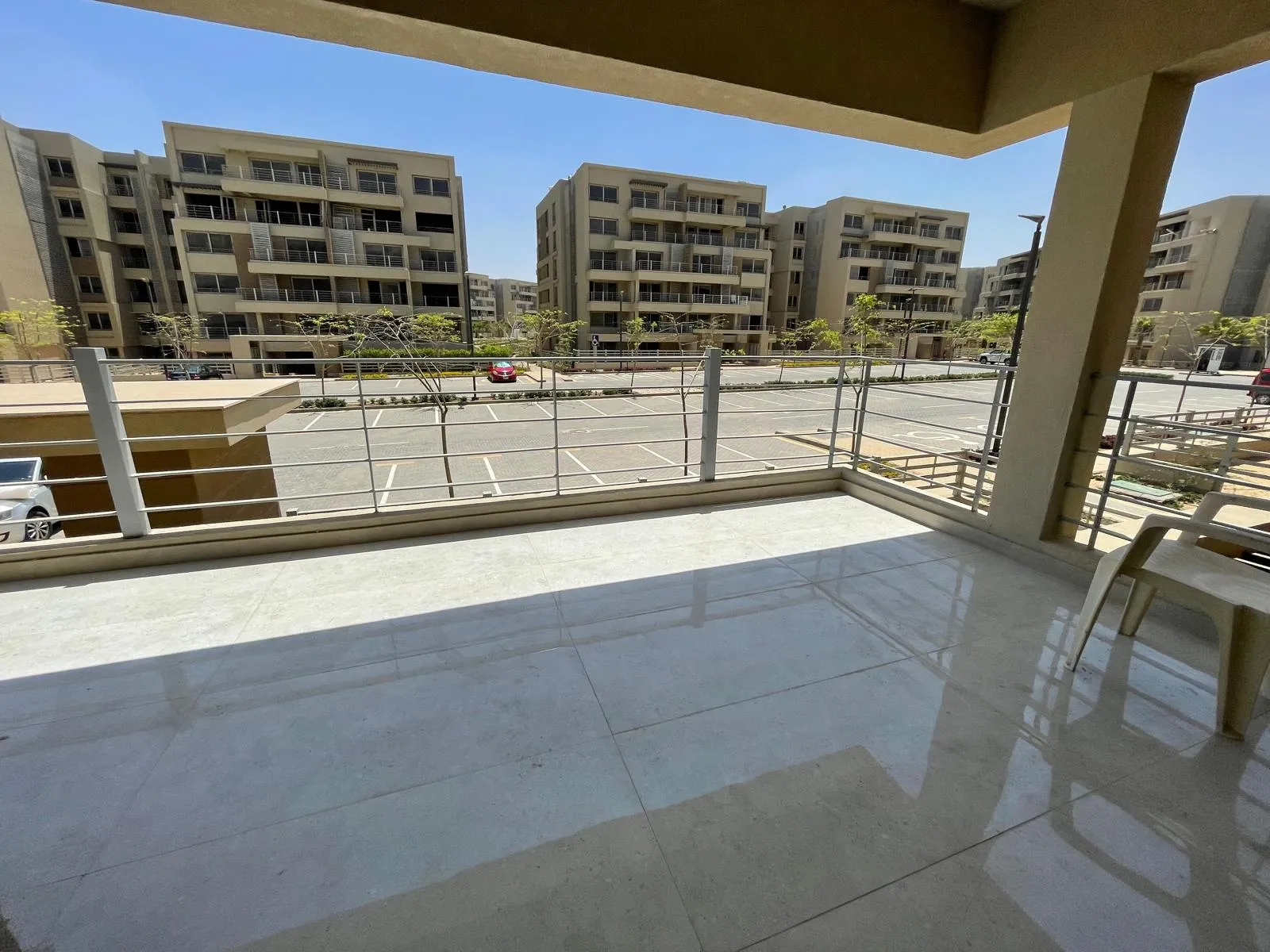 Covered terrace with a glass railing overlooking residential buildings and a car park - apartment in Capital Gardens Next to Madinaty, Mostaqbal City