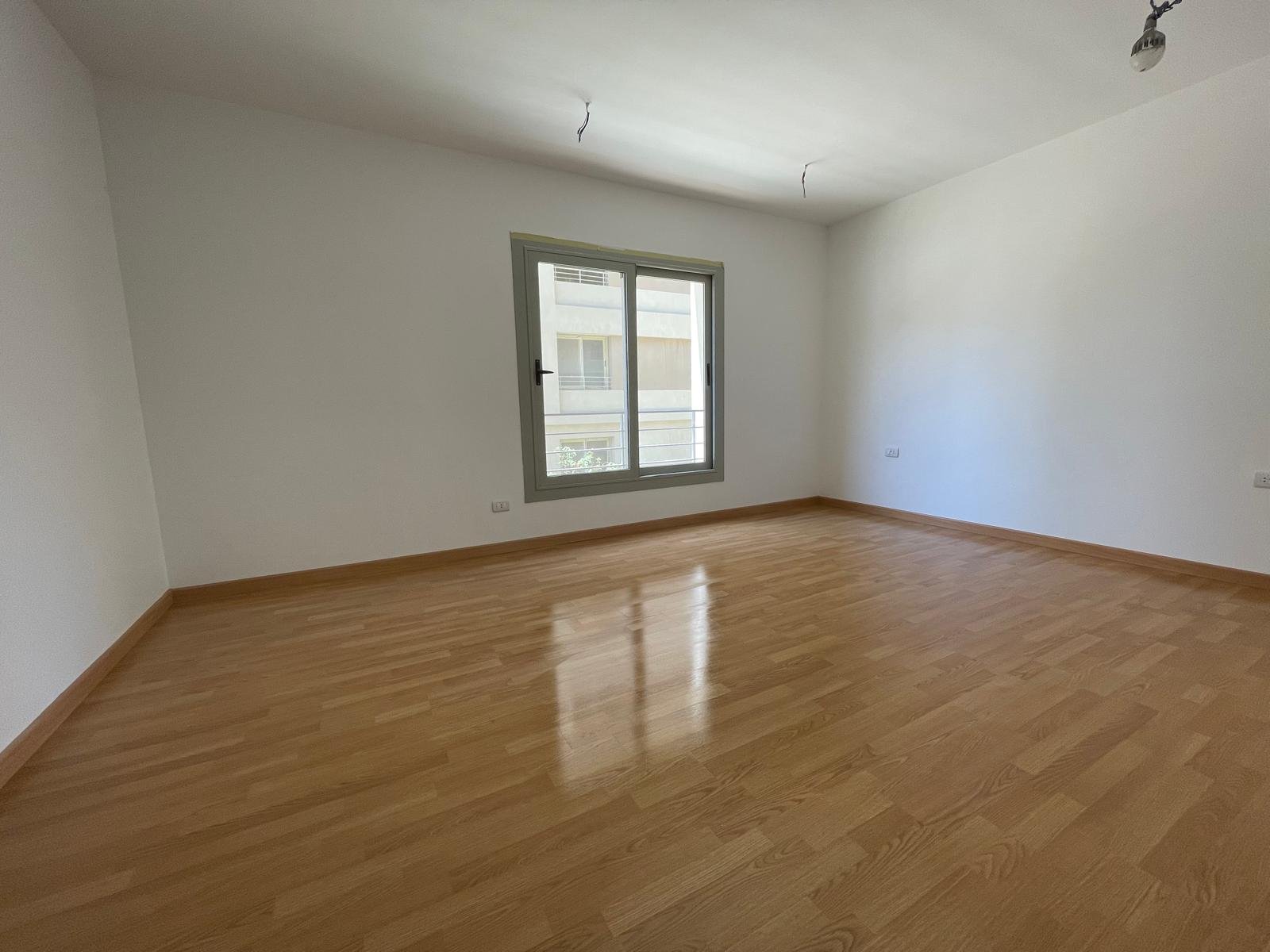 Bright empty room with a grey-framed window and a wooden floor - apartment in Capital Gardens Next to Madinaty, Mostaqbal City
