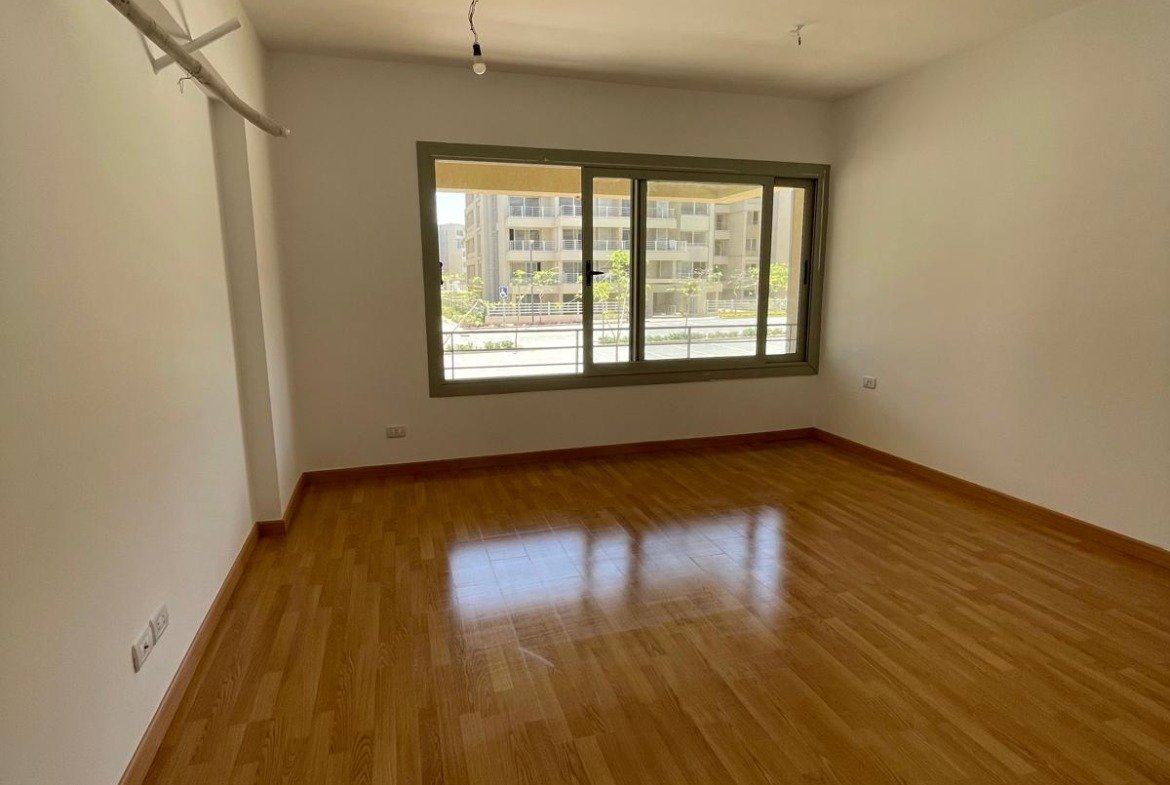 Empty bedroom with a window and a wooden floor - apartment in Capital Gardens Next to Madinaty, Mostaqbal City