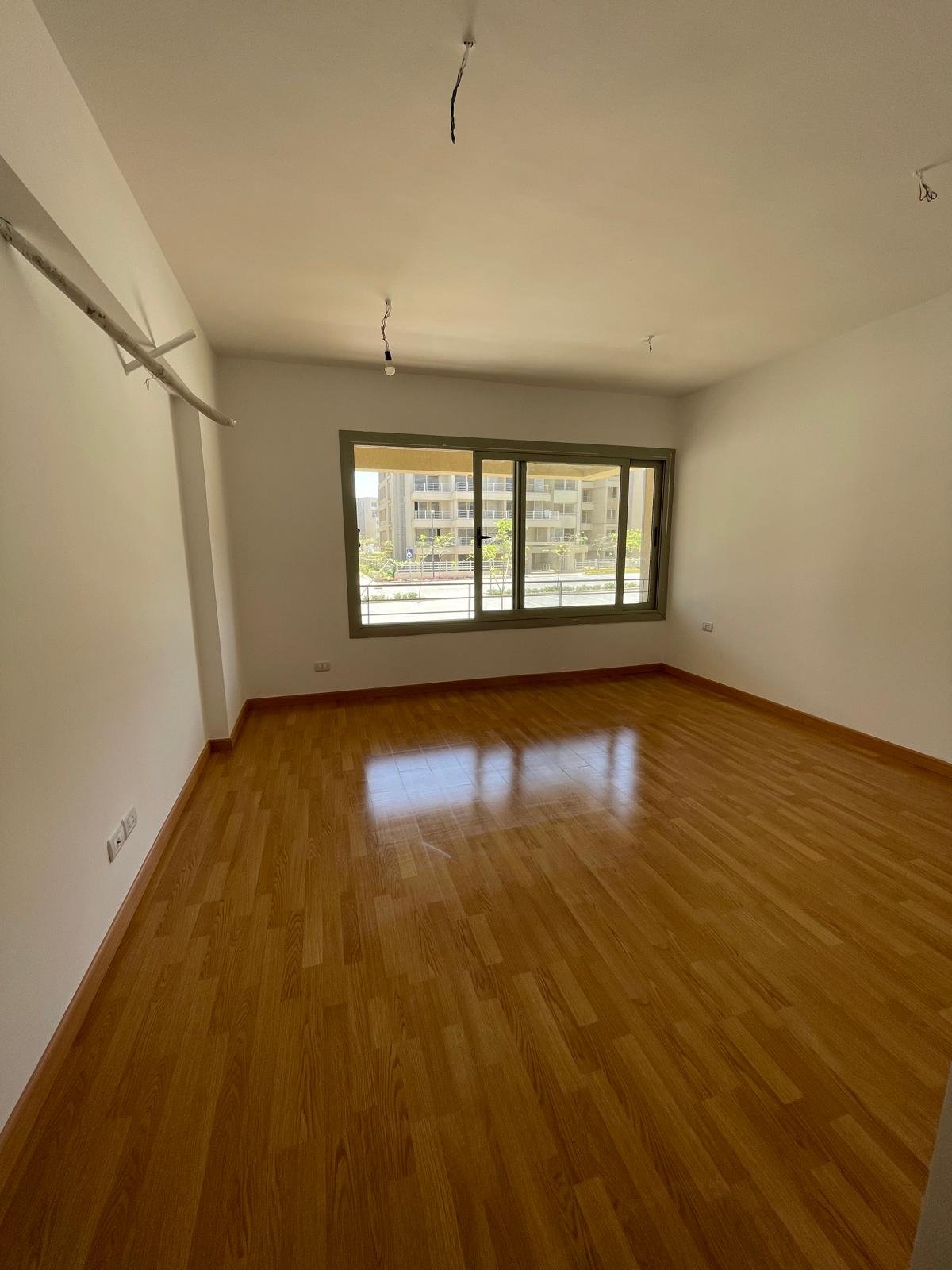 Empty bedroom with a window and a wooden floor - apartment in Capital Gardens Next to Madinaty, Mostaqbal City