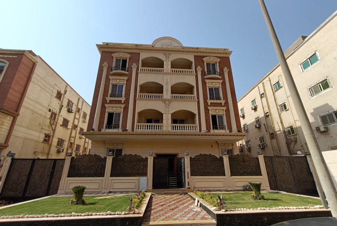 Wide front view of a terracotta apartment building with small lawns - apartment in Gharb Arabella, 5th Settlement