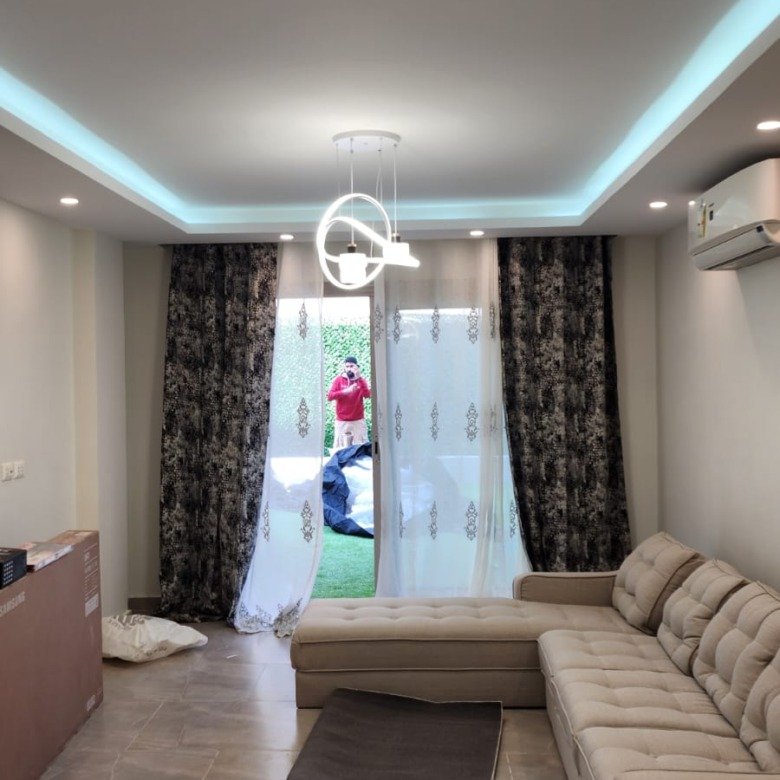 Living room with a large grey corner sofa and a ceiling light strip - apartment in Galleria Moon Valley, 5th Settlement