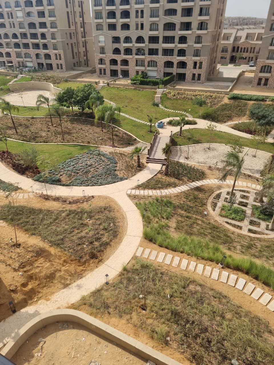 Garden with curved sand-coloured paths seen from a balcony - apartment in Green Square, Mostaqbal City