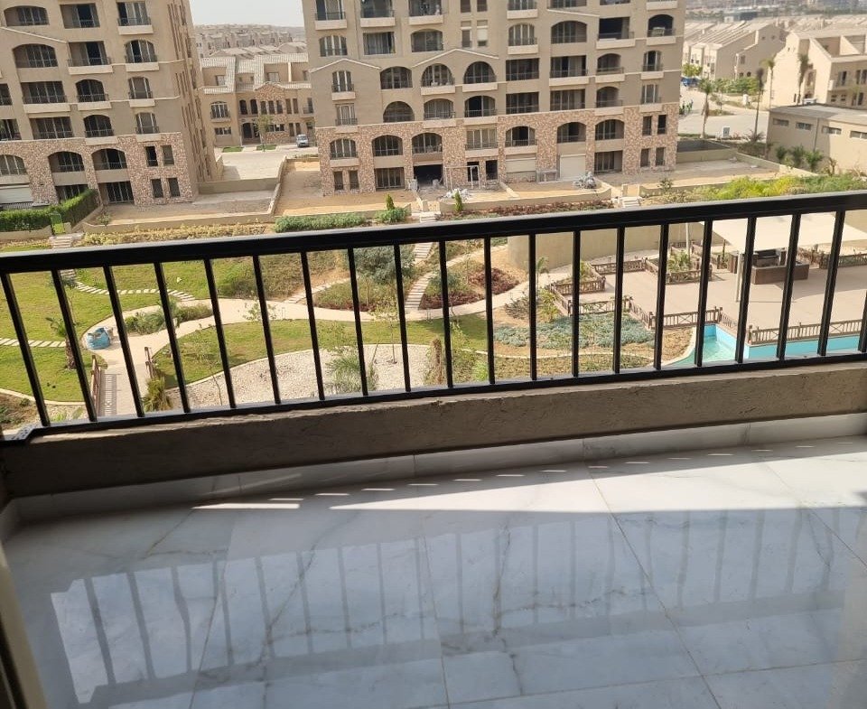 Large balcony with a black railing and a polished floor facing the garden - apartment in Green Square, Mostaqbal City