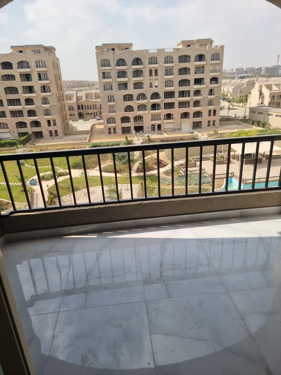 Large balcony with a black railing and a polished floor facing the garden - apartment in Green Square, Mostaqbal City