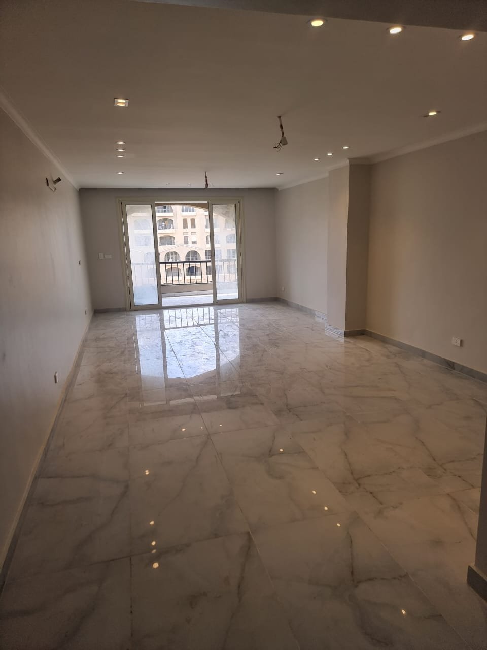 Empty living room with a polished marble floor and a balcony door - apartment in Green Square, Mostaqbal City