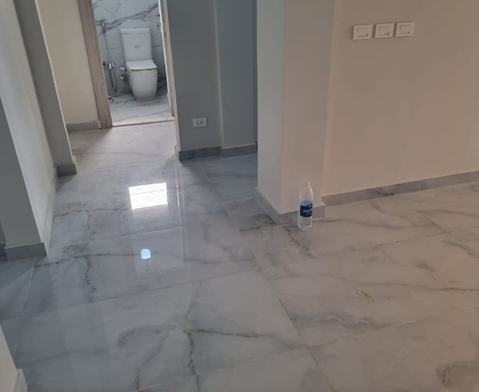 Hallway with white marble floors and a bathroom door in the distance - apartment in Green Square, Mostaqbal City