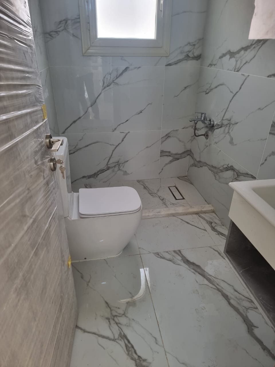 Bathroom with marble-look walls, a wall-hung toilet and a vanity - apartment in Green Square, Mostaqbal City