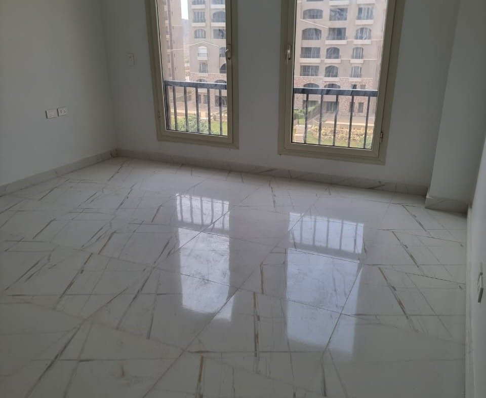 Empty room with two tall windows and a glossy tiled floor - apartment in Green Square, Mostaqbal City