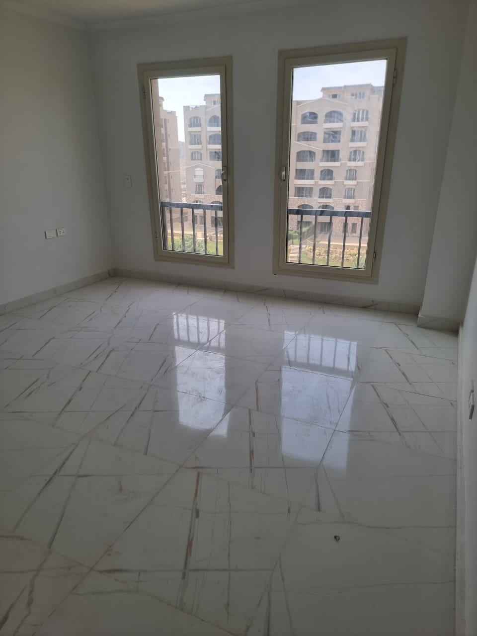 Empty room with two tall windows and a glossy tiled floor - apartment in Green Square, Mostaqbal City