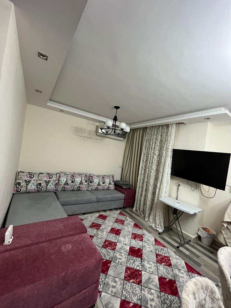 madinaty-apt-89-09 غرفة جلوس بغطاء كنب أحمر منقوش وتلفزيون على الحائط - شقة في مدينتي، القاهرة الجديدة