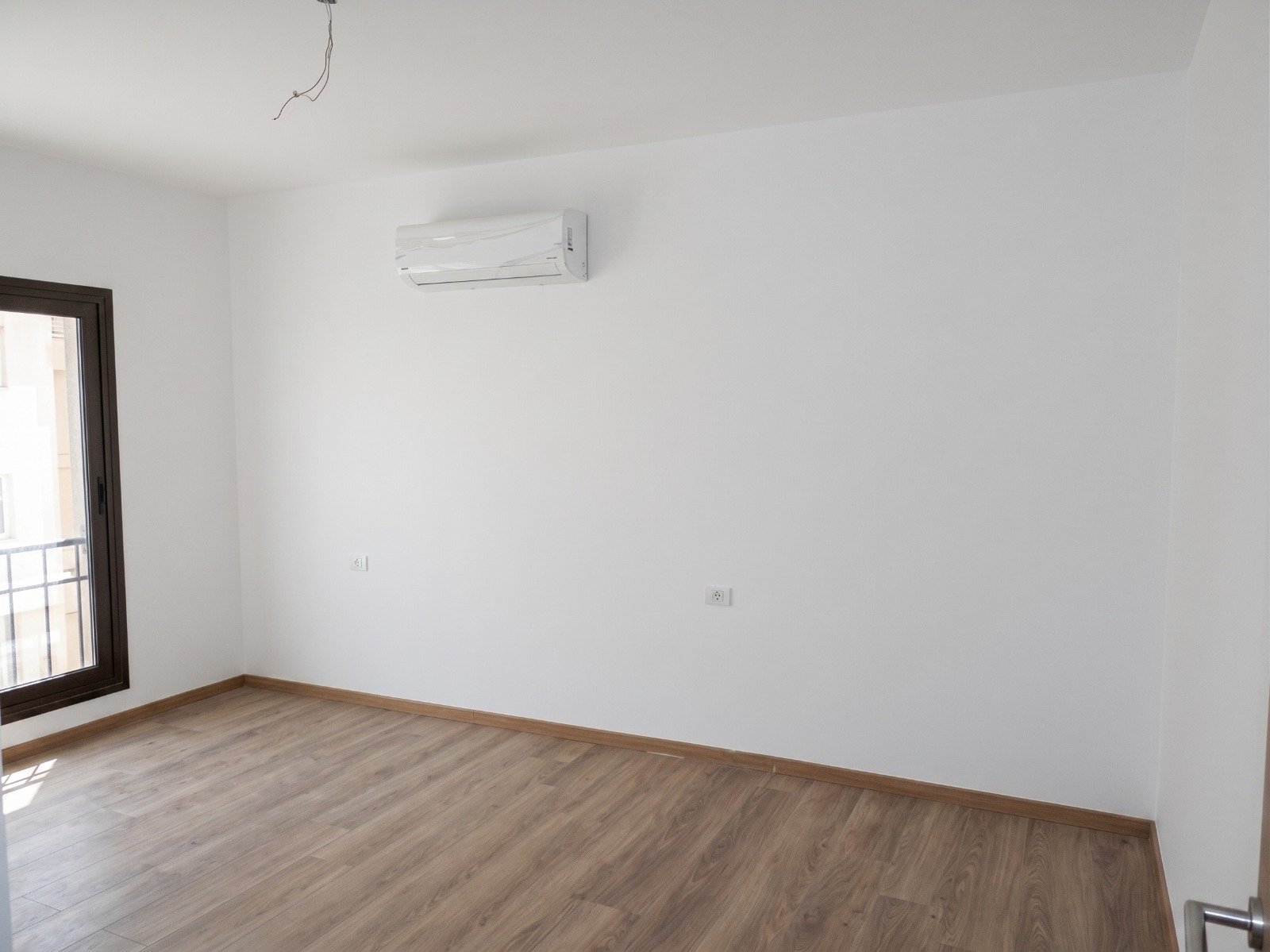 moon-residences-5th-square-bedroom-wood Empty bedroom with balcony door and air conditioner - apartment in Moon Residence, Fifth Square, New Cairo