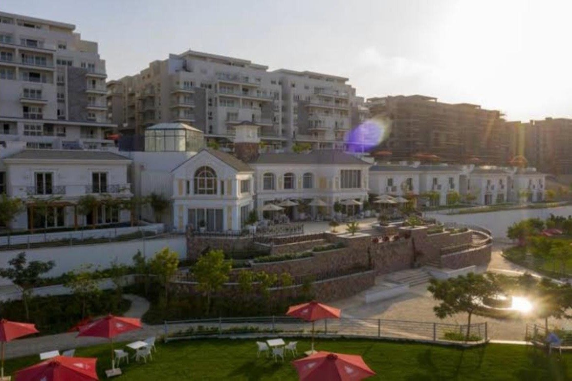 Clubhouse and landscaped lawn at sunset with red umbrellas - apartment in Mountain View iCity, New Cairo
