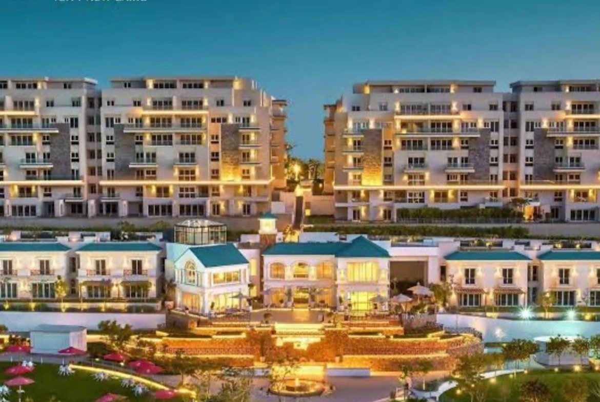 Illuminated apartment blocks and clubhouse at dusk in a promotional image - apartment in Mountain View iCity, New Cairo