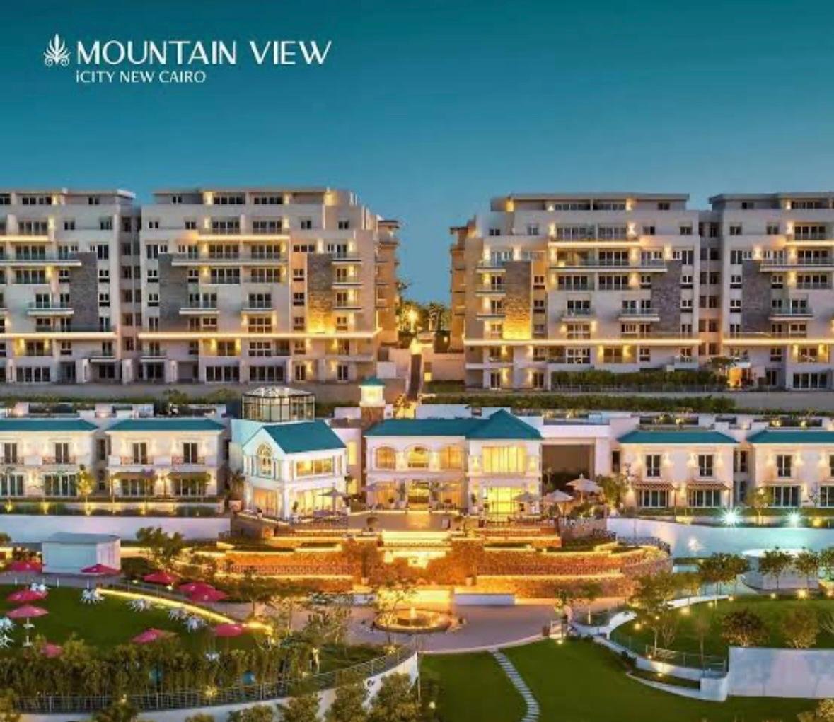 mvic525-u20 Illuminated apartment blocks and clubhouse at dusk in a promotional image - apartment in Mountain View iCity, New Cairo