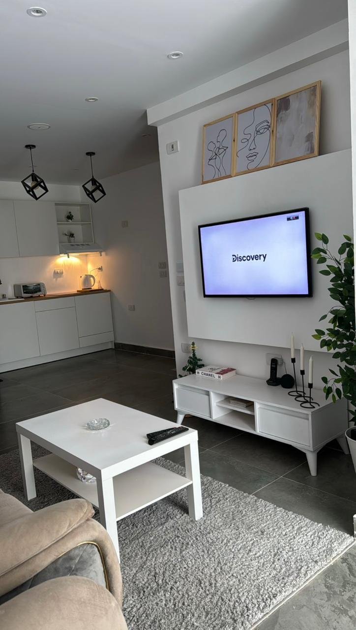 mvic525-u8 TV wall with a white coffee table and kitchenette behind - apartment in Mountain View iCity, New Cairo