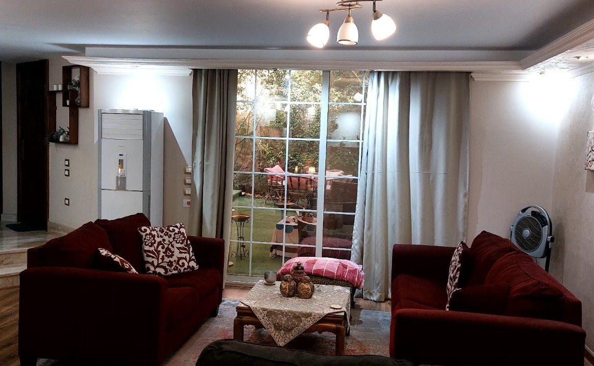 Living room with red sofas and garden-view curtains - duplex in One Piece, New Cairo