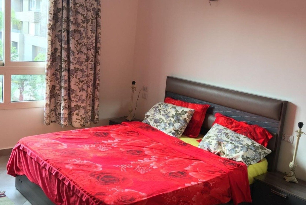 Bedroom with a red bedspread, curtains and a patterned rug - apartment in Park View, New Cairo
