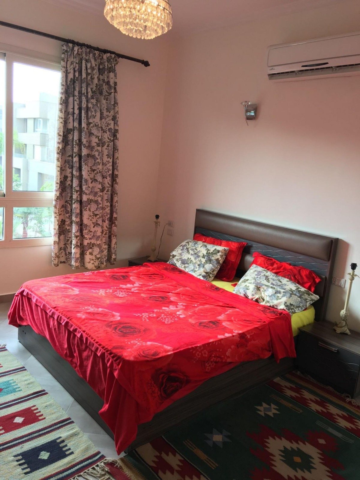 Bedroom with a red bedspread, curtains and a patterned rug - apartment in Park View, New Cairo