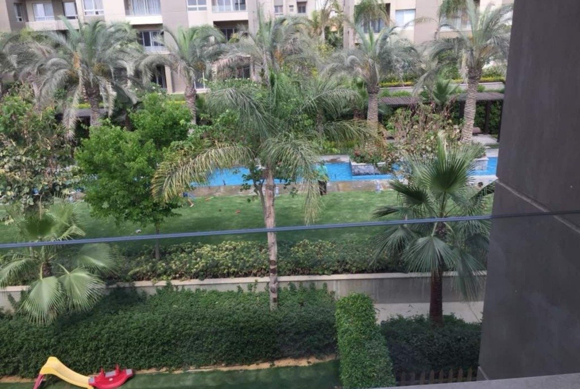 Pool and palm garden viewed from a ground-floor terrace - apartment in Park View, New Cairo