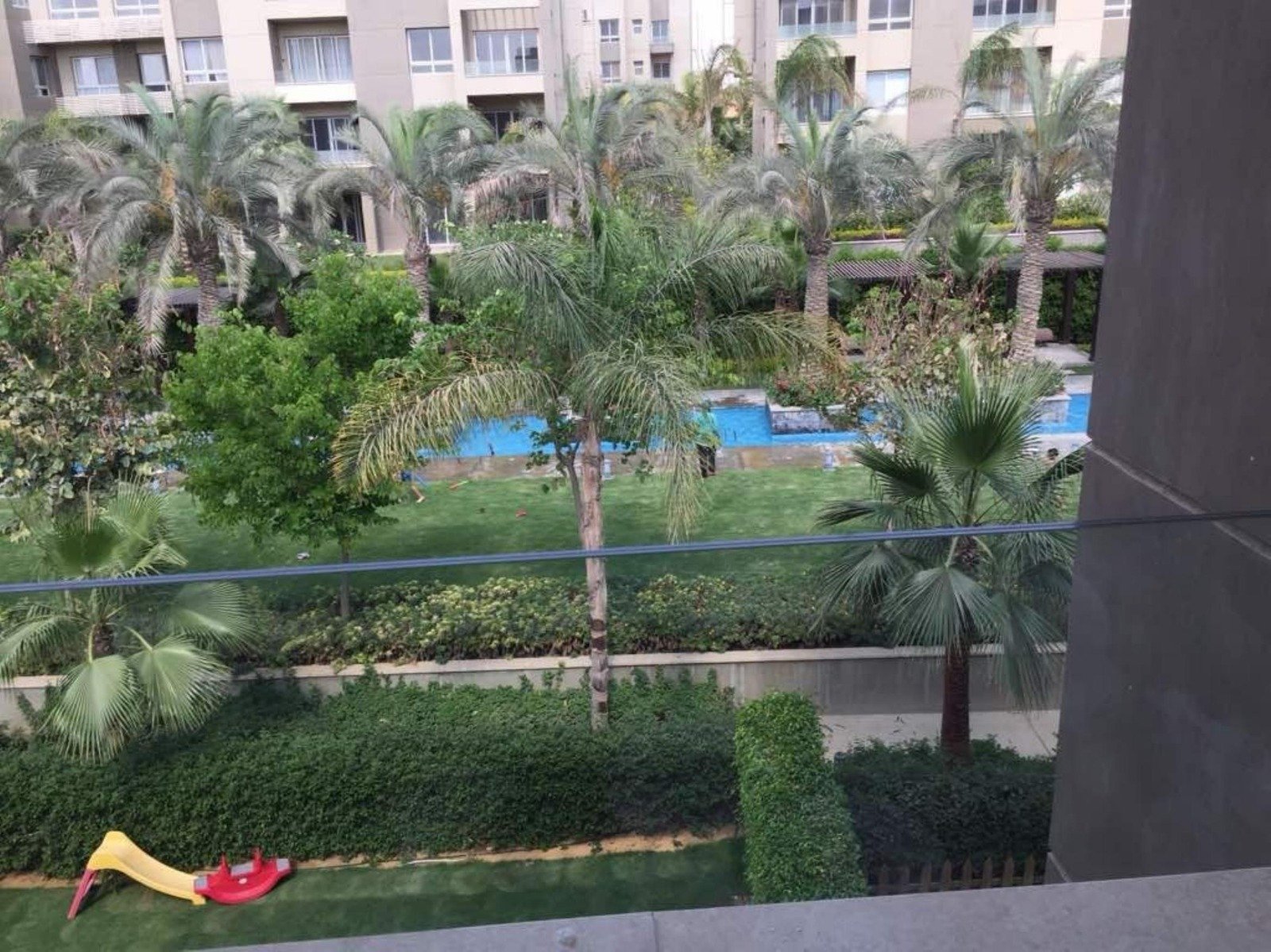 Pool and palm garden viewed from a ground-floor terrace - apartment in Park View, New Cairo