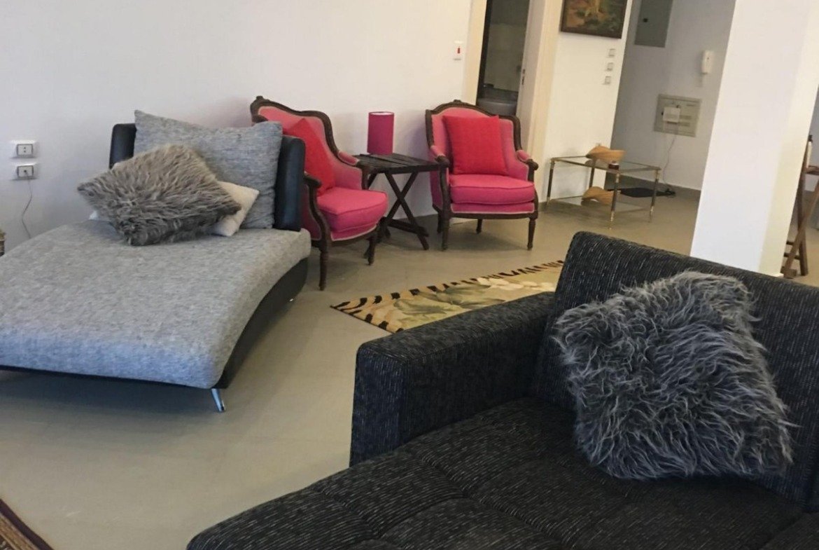 Open living area with a black corner sofa and red chairs - apartment in Park View, New Cairo