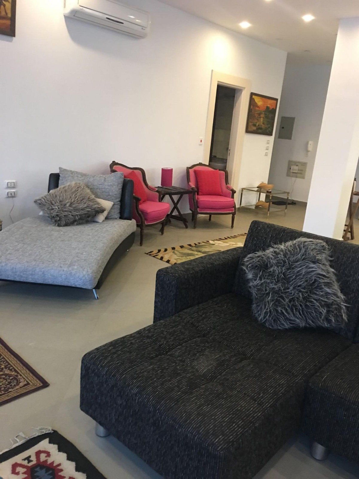 Open living area with a black corner sofa and red chairs - apartment in Park View, New Cairo