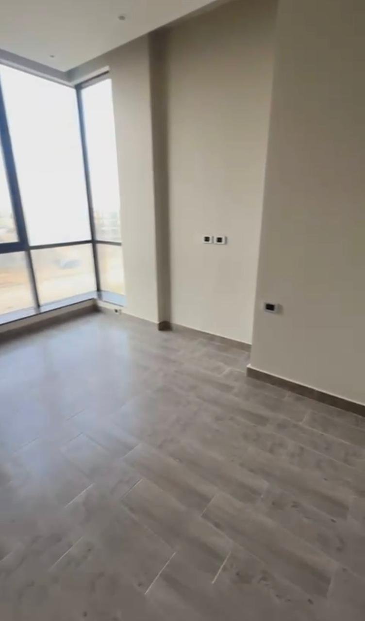 Bright empty room with a tall window and wood-look floor - apartment in El Patio Oro, New Cairo