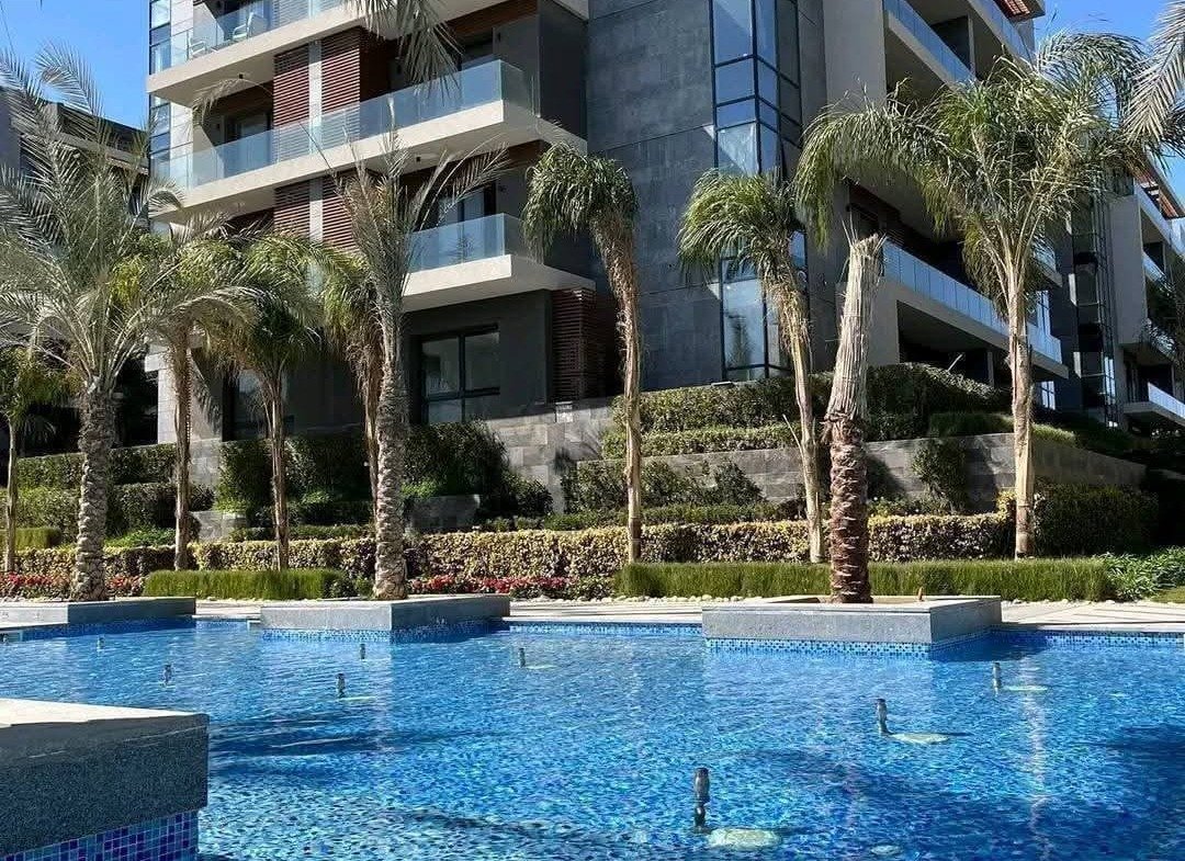 Apartment building rising behind a swimming pool and palm trees - apartment in El Patio Oro, New Cairo