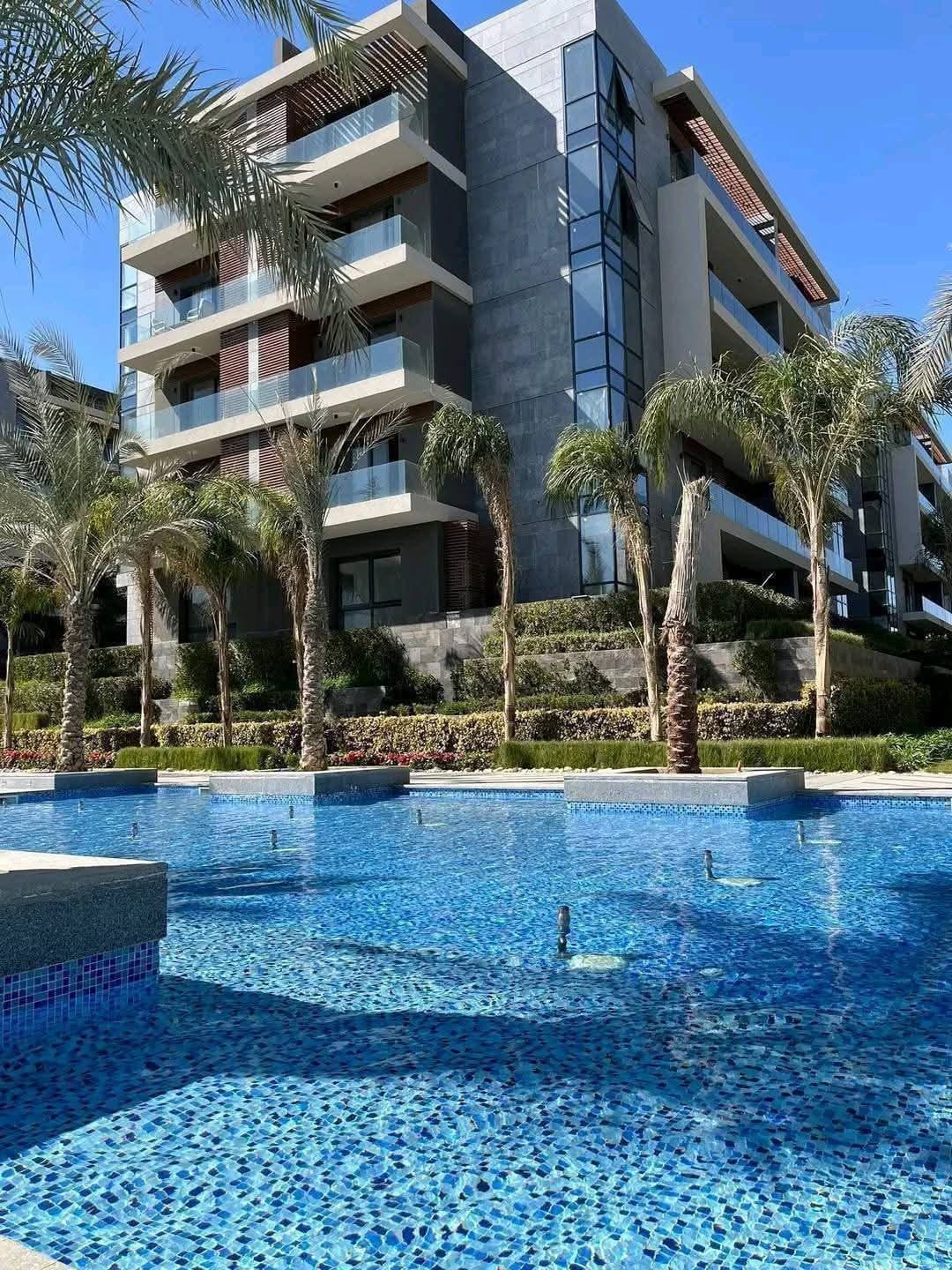 Apartment building rising behind a swimming pool and palm trees - apartment in El Patio Oro, New Cairo