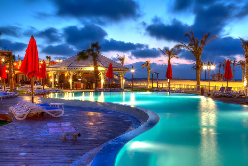 Resort pool glowing at dusk with red parasols and palm trees - chalet in Porto Matruh, North Coast