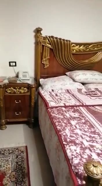 Bedroom with a carved wooden headboard and red bedding - apartment in South of Academy, 5th Settlement