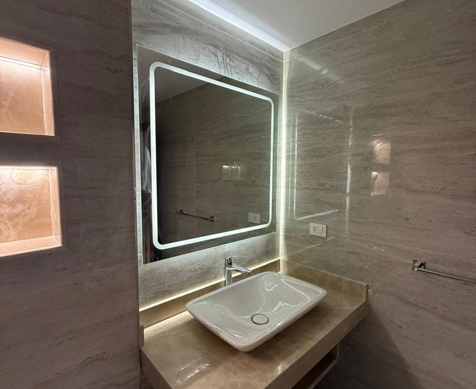 Washbasin and mirror with soft backlighting on a stone wall - apartment in Sakan Compound, New Cairo