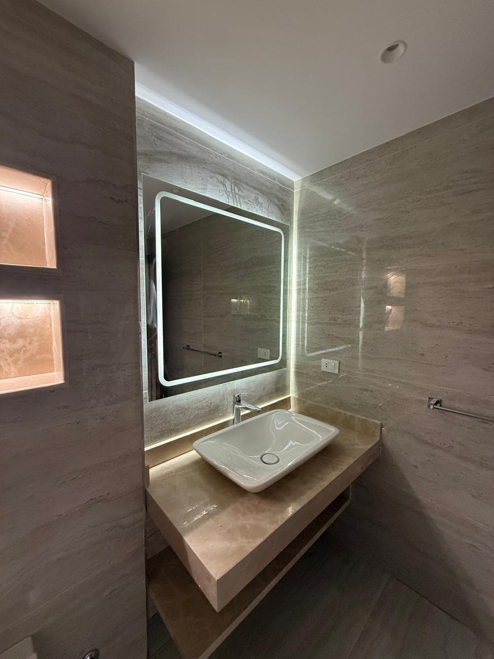 Washbasin and mirror with soft backlighting on a stone wall - apartment in Sakan Compound, New Cairo