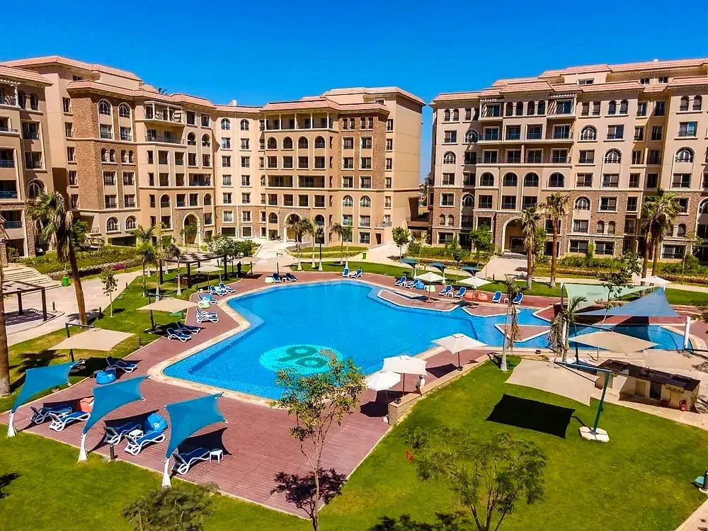 Large lagoon-shaped pool with loungers and umbrellas among apartment buildings - apartment in Serenity 90 Avenue, New Cairo